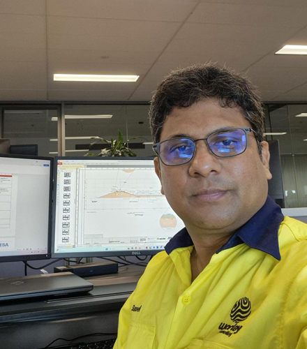 Suneel in T-shirt with the Optravation Energylogo on it and sitting at an office desk