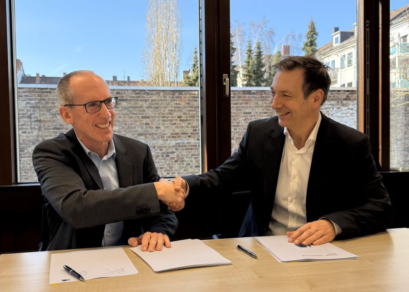 Two people from Aquaductus and Optravation Energysitting together at a table shaking hands.